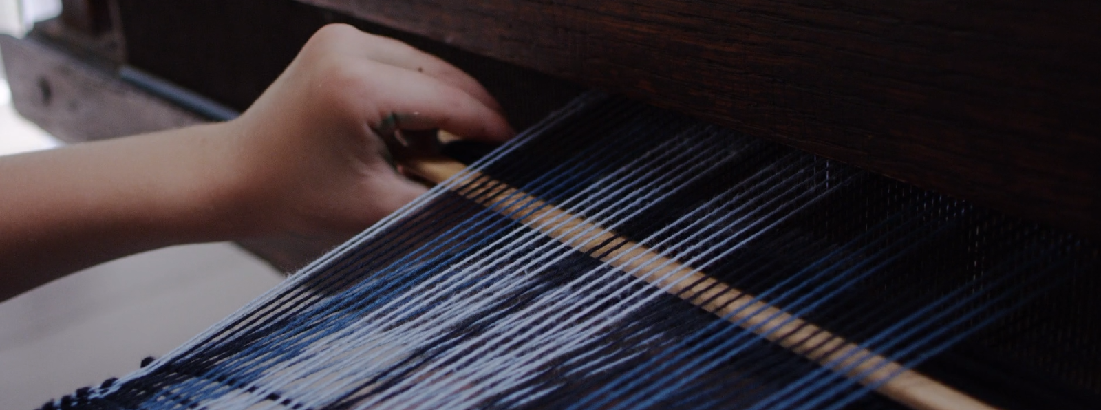 Close up of a child's hand weaving on a loom.