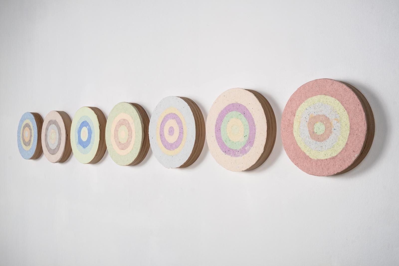 Cast paper from recycled screenprints on plywood rounds of similar size in a row.