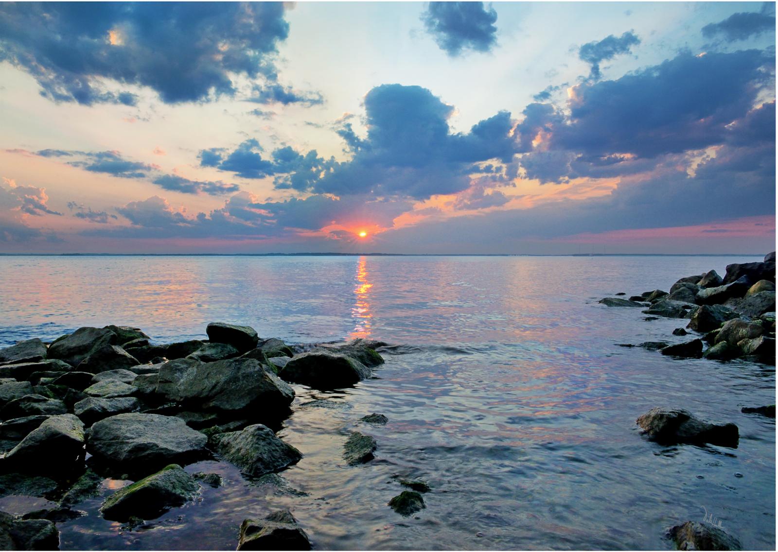 A tangerine sunburst appears as the sun sets over glassy waters on the Chesapeake.