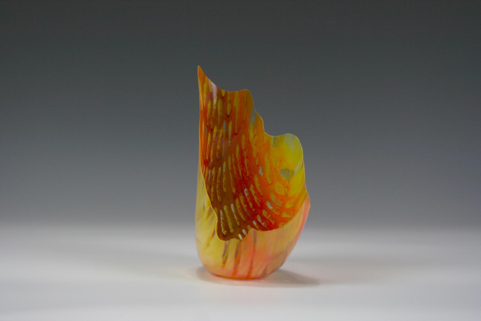 This piece is an orange, yellow and red thin-walled drop vessel with an amorphous edge. This piece was inspired by the vibrant colors and textures of torch lily flowers I saw at a botanical garden in Australia.