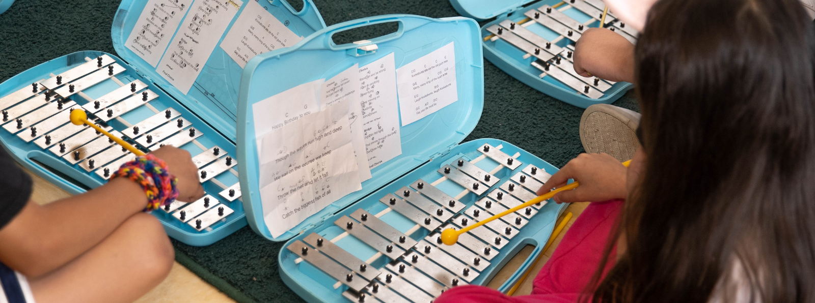 Closeup of three children playing the xylophone.