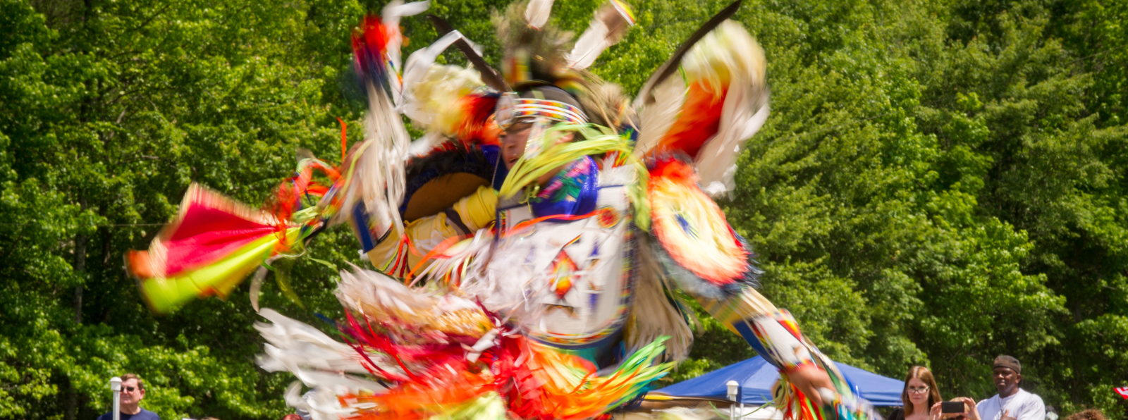 An Indigenous person in a ceremonial outfit is dancing for a crowd.