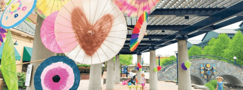 A cluster of colorful painted paper umbrellas installed outdoors next to a river