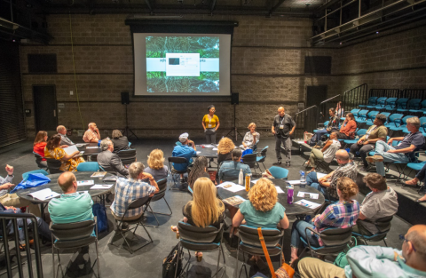 A room of seated people facing forward looking at a presentation