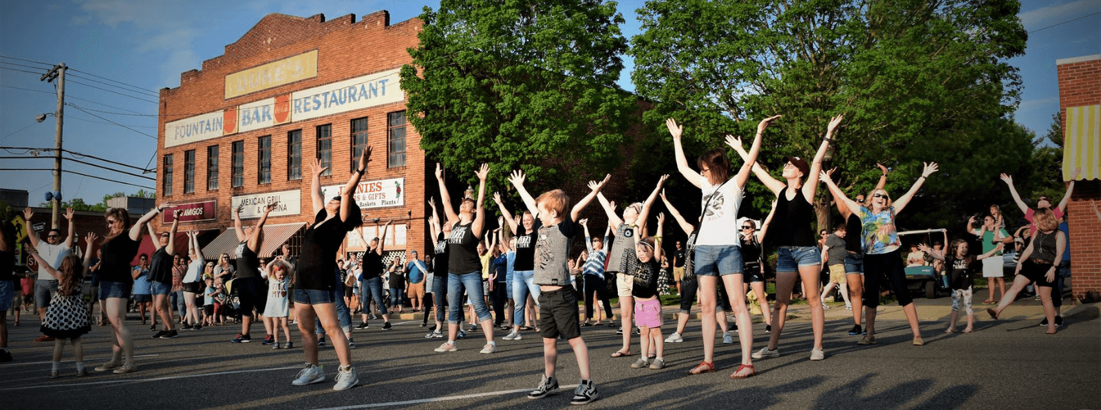 Youth and adults outdoors with their arms extending up participating in a flash mob dance