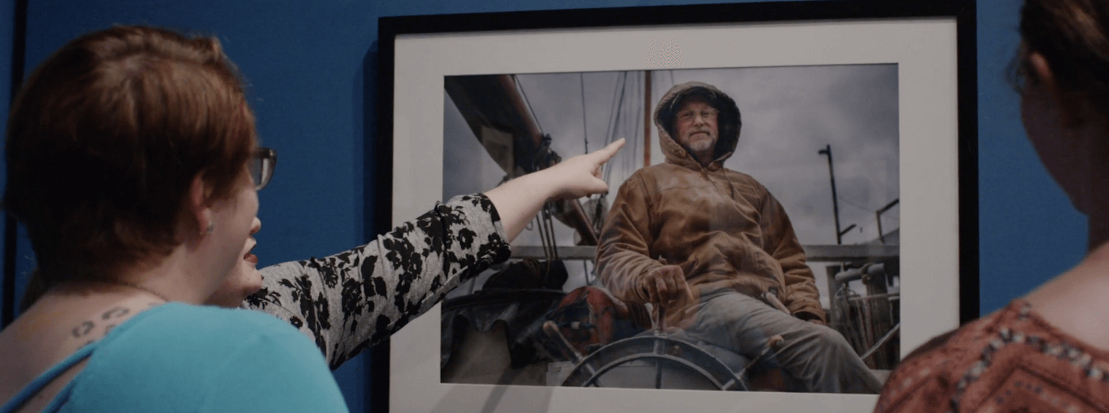 A person in a gallery points to a painting of a person on a boat