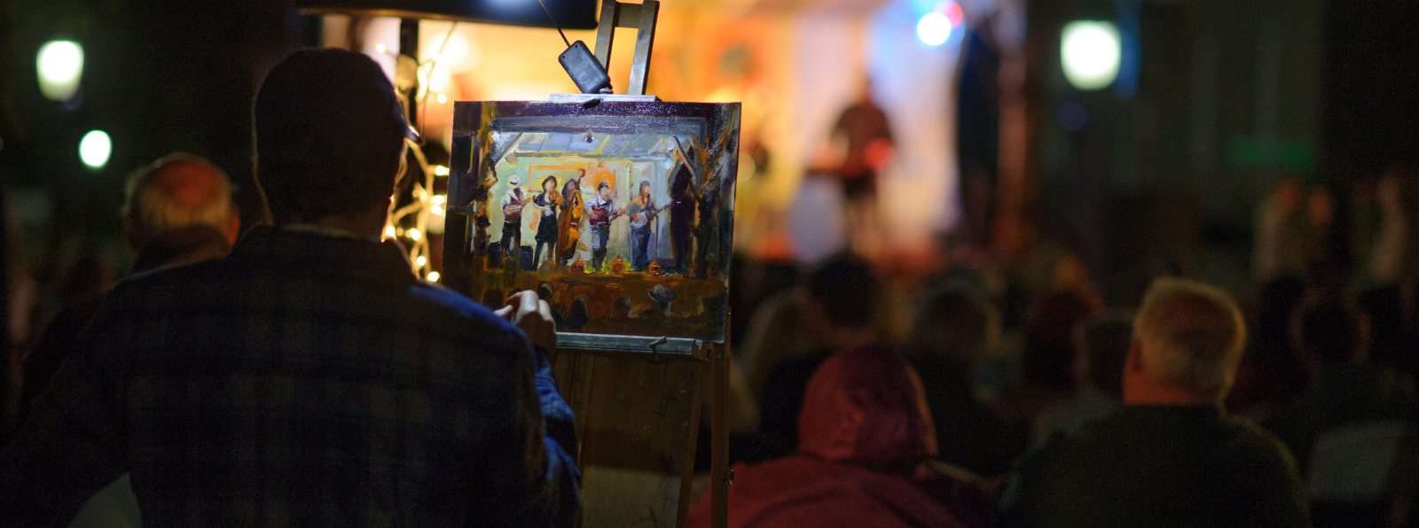 A person at an easel is painting a crowd watching a performance on stage.
