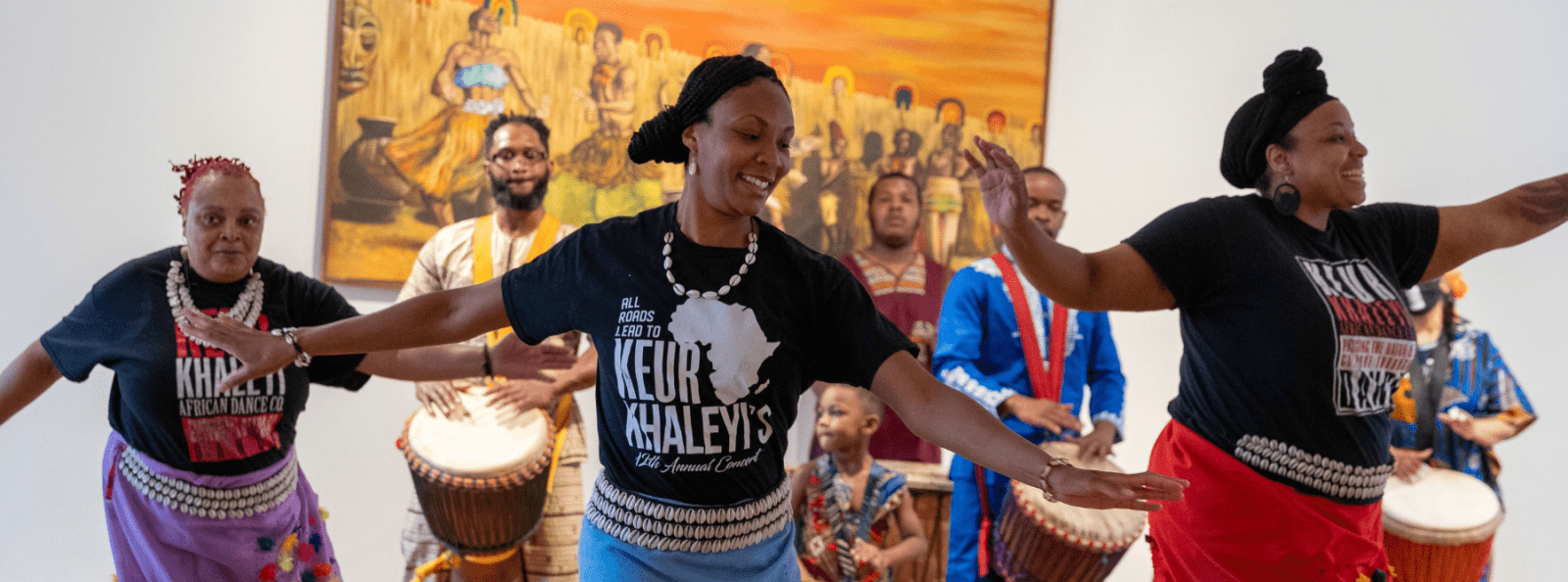 3 dancers performing to live drum circle behind them. 