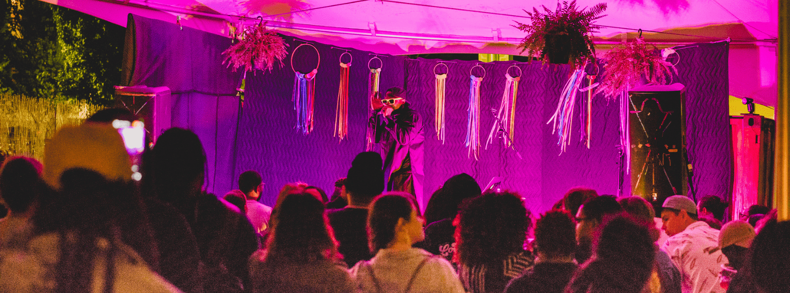 Performer lit with purple stage lights above audience with microphone in hand. Bromo Arts District header image.