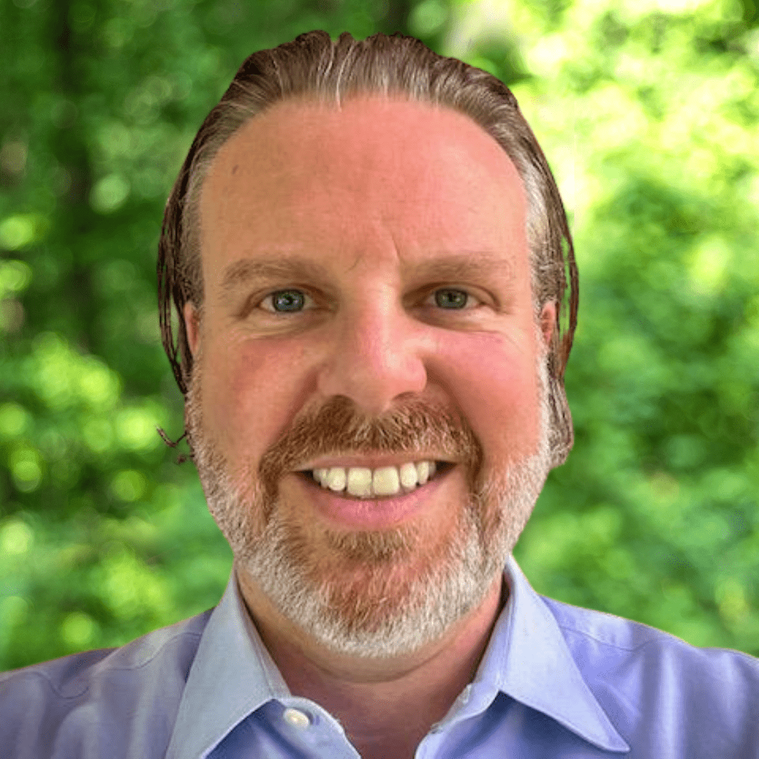 Brad Bittner Headshot. Man with beard smiling at camera with light blue collared shirt on