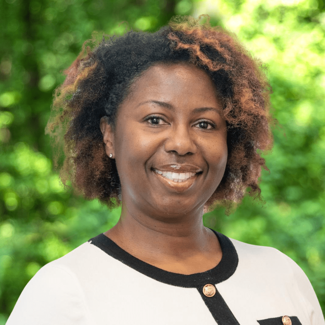 Leslie Gillard headshot, women smiling with white shirt, green forest background