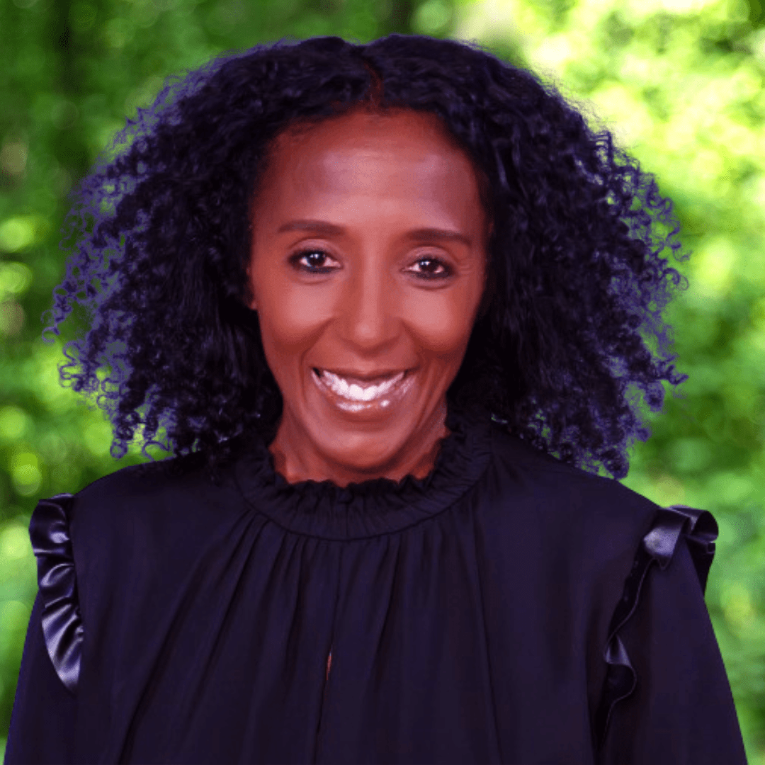 Smiling woman with curly black hair, wearing a black jacket and looking directly at the camera.