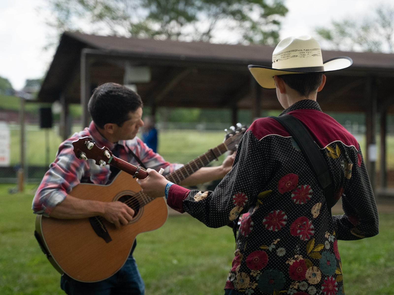 Two musician playing guitars outside by a pavillion