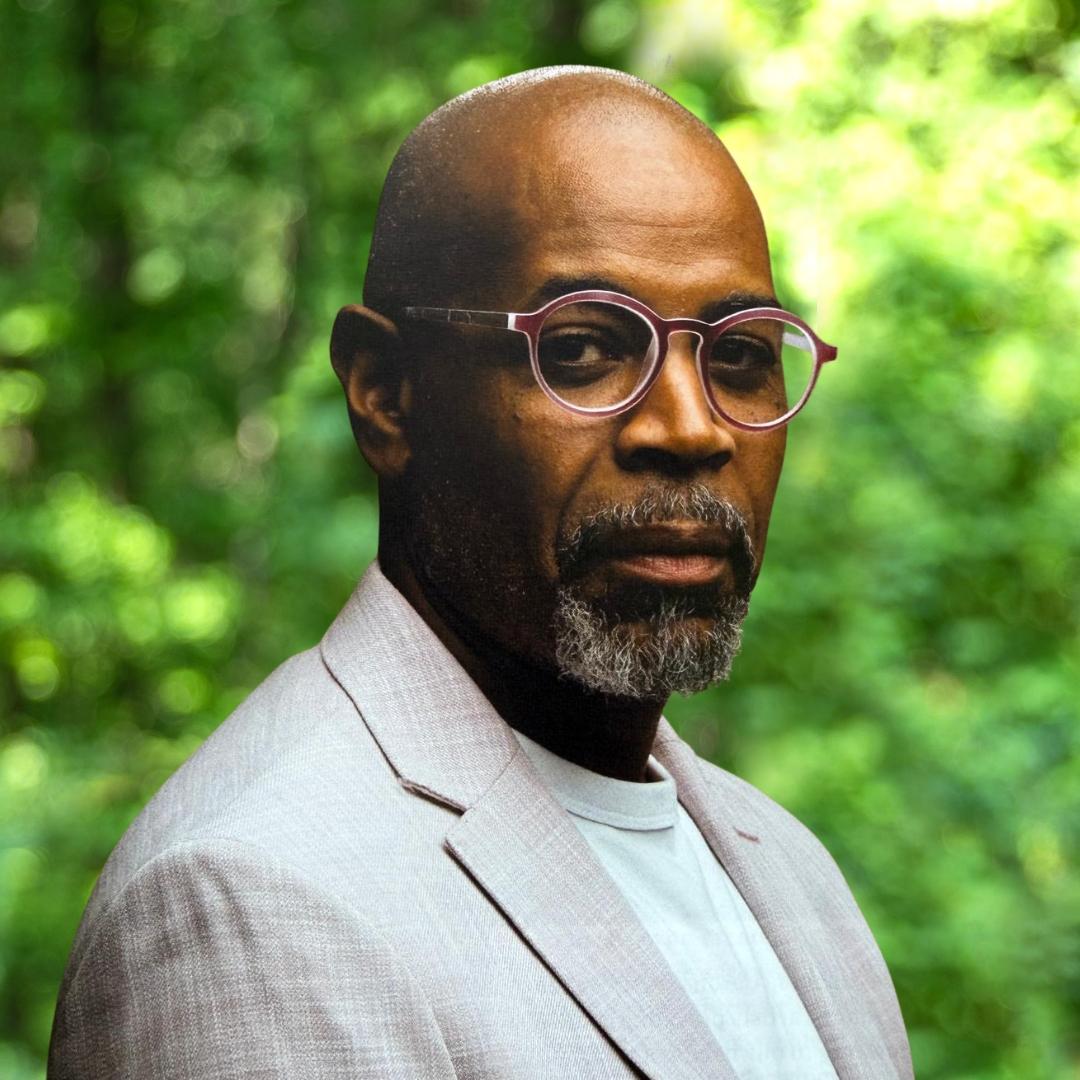 Jason Steer headshot - Man with beard and glasses, wearing a light color suit and looking at camera intensely
