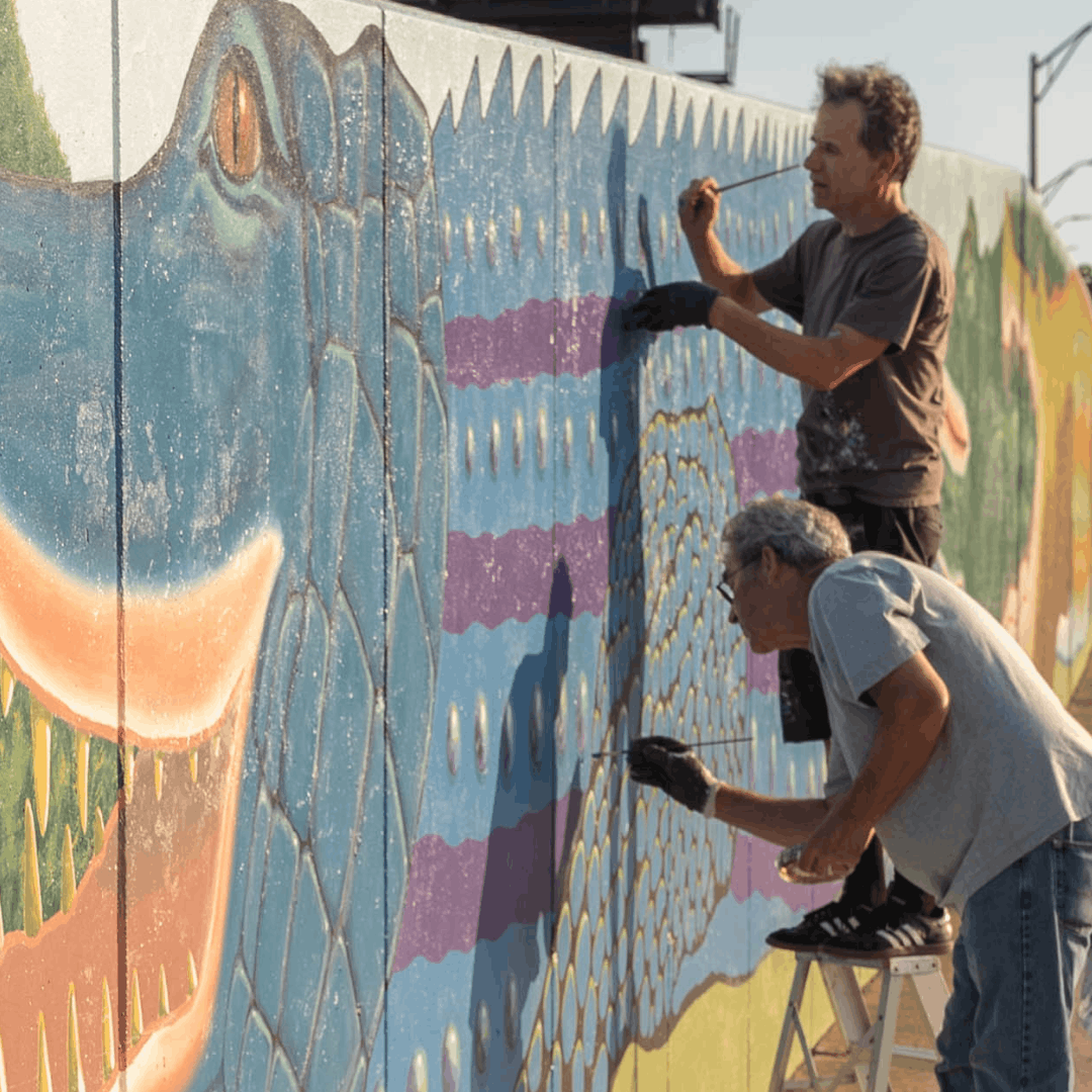 Two men painting an outdoor mural in Baltimore City. 