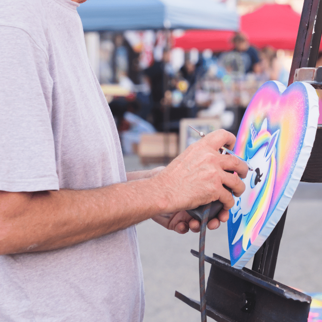 Airbrush artists painting a colorful heart canva with a rainbow unicorn.