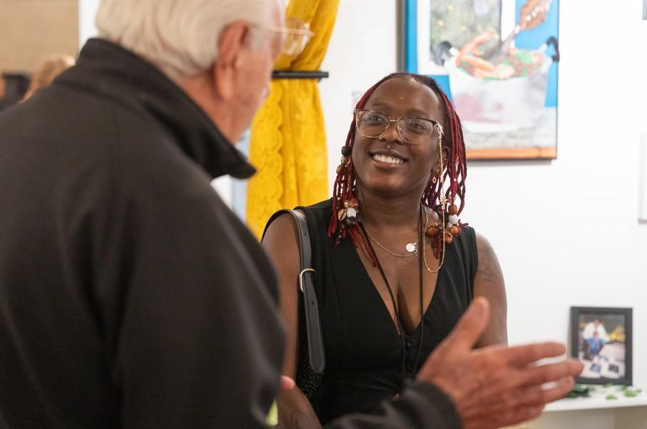 Woman with glasses and black and red braids smiling at man with white hair as he talks to her