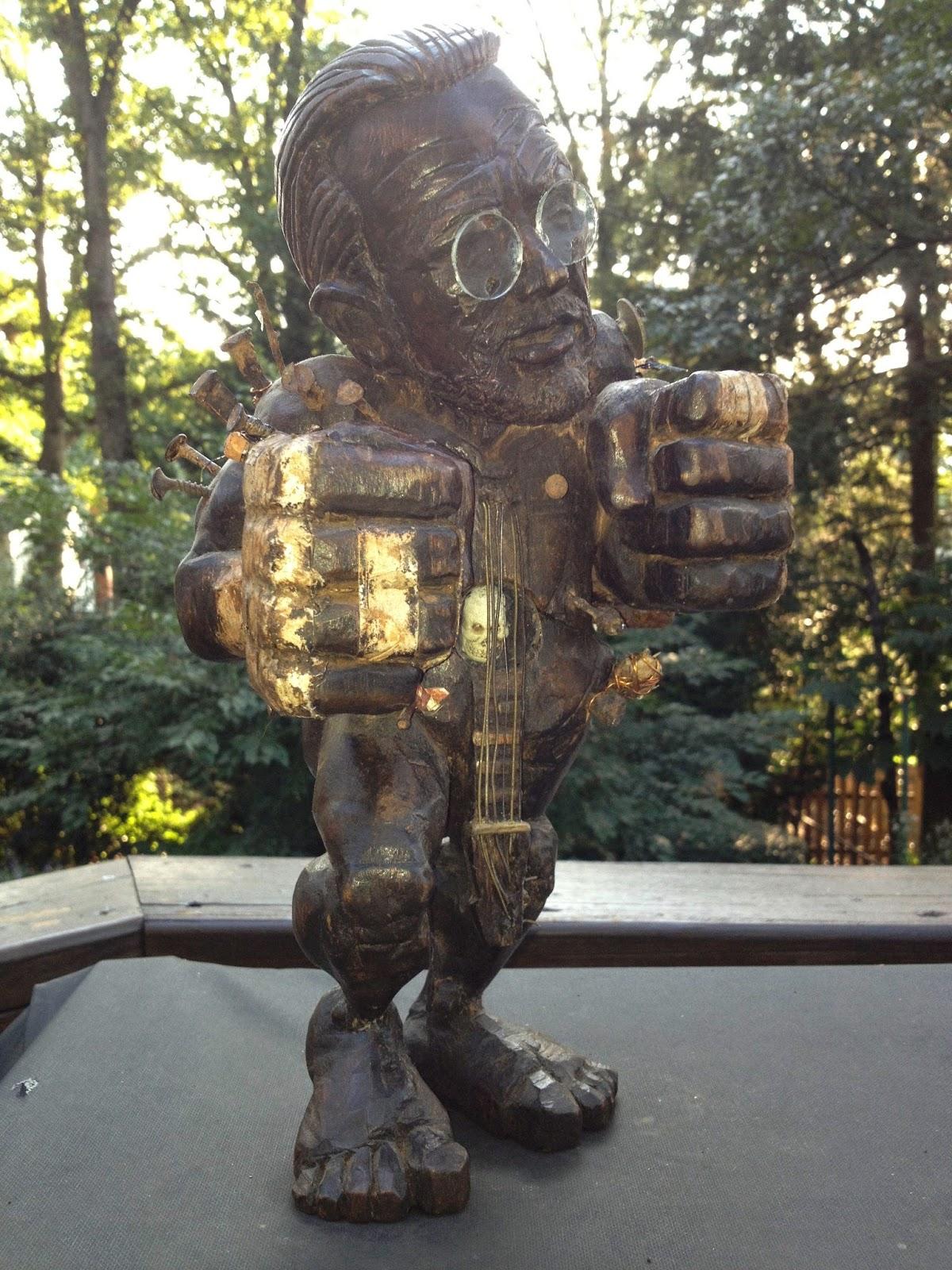 Warren Zevon – a perseverance/acceptance of mortality nkisi
Zevon is presented as a boxer, at the end of a fight, with his hands still taped and bloodied, (alluding to his creative persona most explicit in his song title, Piano Fighter, and, perhaps, to his father’s influential though short career as a professional boxer). Zevon’s cocked eyebrow suggests the ironic attitude that completed his persona. Zevon’s torso juxtaposes the death’s head in a mirror box with the virility of a rock guitar neck and strings. The mbau refer to Zevon’s ironic dance with death throughout his life and work and the cigarettes/lung cancer which finally killed him.