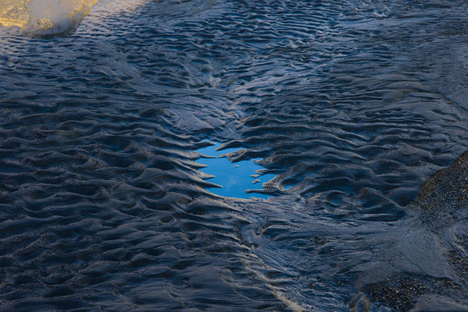 Sand in the shadow of the Canada Glacier beside the Lake Hoare field camp during the brief melt season, a puddle reflecting the clear blue sky of 24-hour daylight at 1:20 a.m.