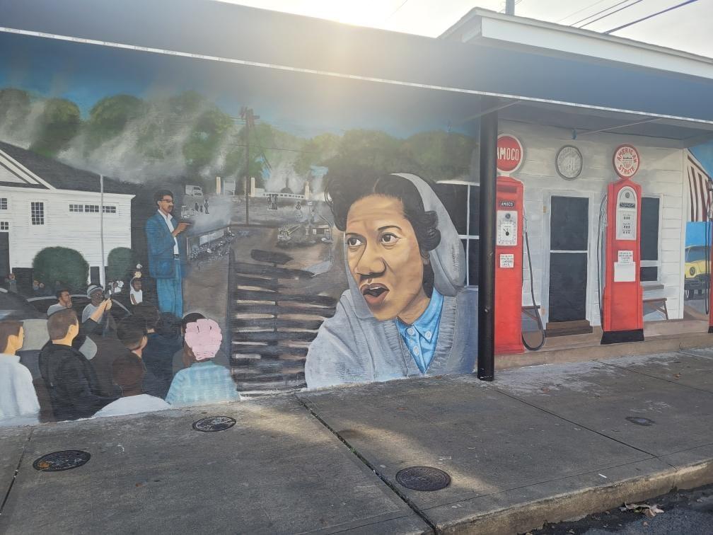 This public art mural was a vision that came from businesses that were on Pine Street before the fire in 1967. It is goal to have a walking mural tour on Pine Street to remember all the black-owned businesses. In this first mural, it shows the gas station that was located at this actual location in 1967. On the left side, a demonstration of the community rallying in front of the Elks Lodge #223 and civil rights leader, Gloria Richardson. In the background, you will see the aftermath of the fire.