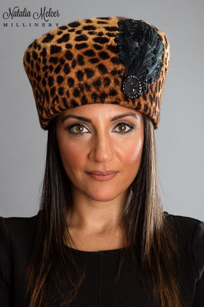 Leopard print fur felt modius crown with black feather and button trim. A sweatband is sewn inside the crown. Hat was made by blocking the felt over a wooden form. One-of-a-kind, handmade hat using traditional millinery techniques.