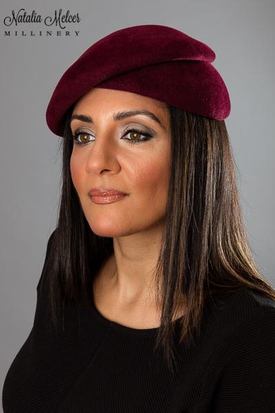 Maroon fur felt beret with a unique folded design. A sweatband is sewn inside the crown and the hat can be secured with an elastic band that goes under the hair. Hat was made by blocking the felt over a wooden form. One-of-a-kind, handmade hat using traditional millinery techniques.