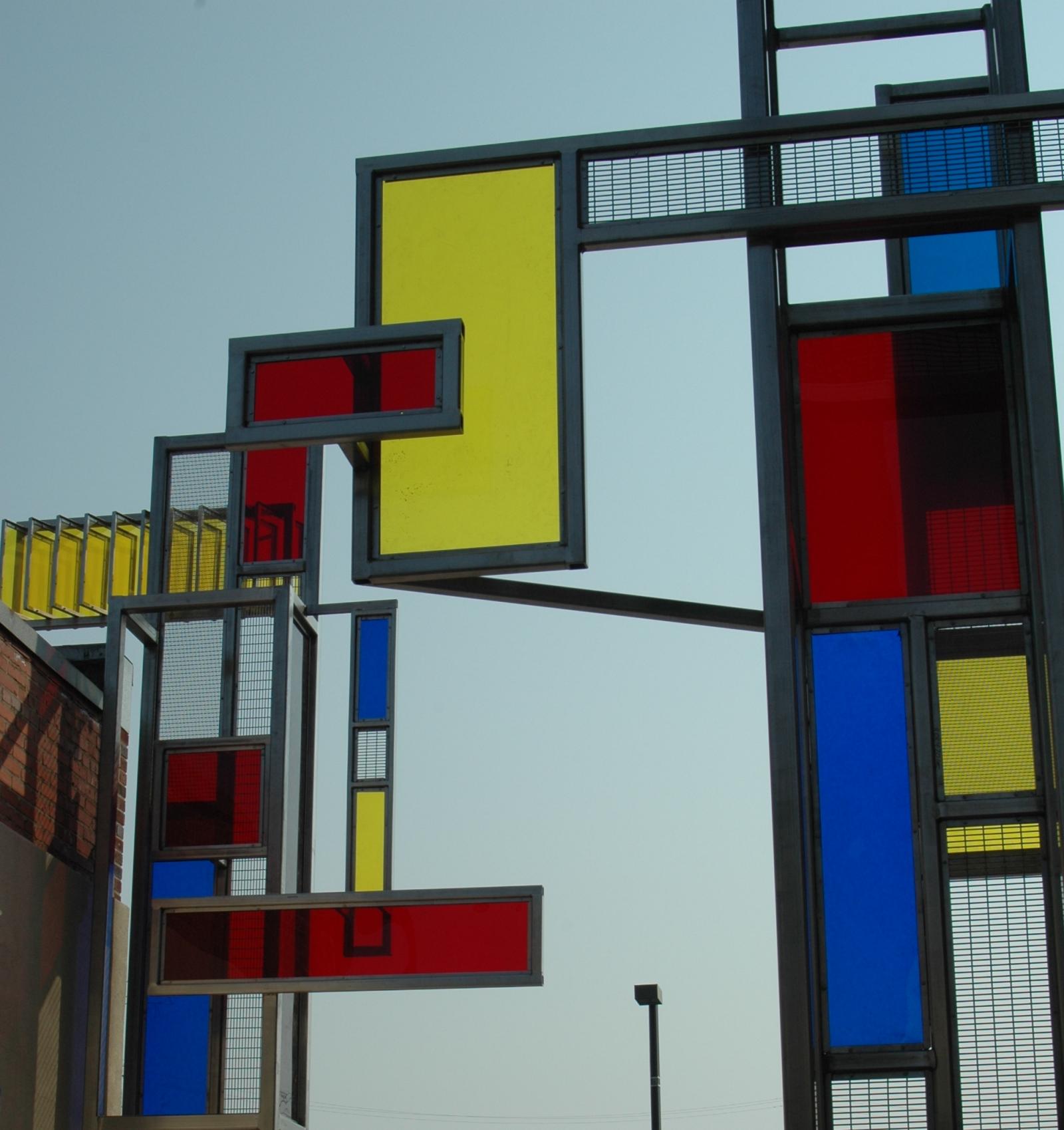  The Windows on Arts Alley were designed in coordination with the revitalizing of    an alley into a pedestrian friendly out-door market with entrances to restaurants and other business.  The structures reflect the industrial history of the area coupled with the new bright colors of the future. With the light of the sun the colored resin reflects Mondrian type patterns onto the walls and paving of the alley.
