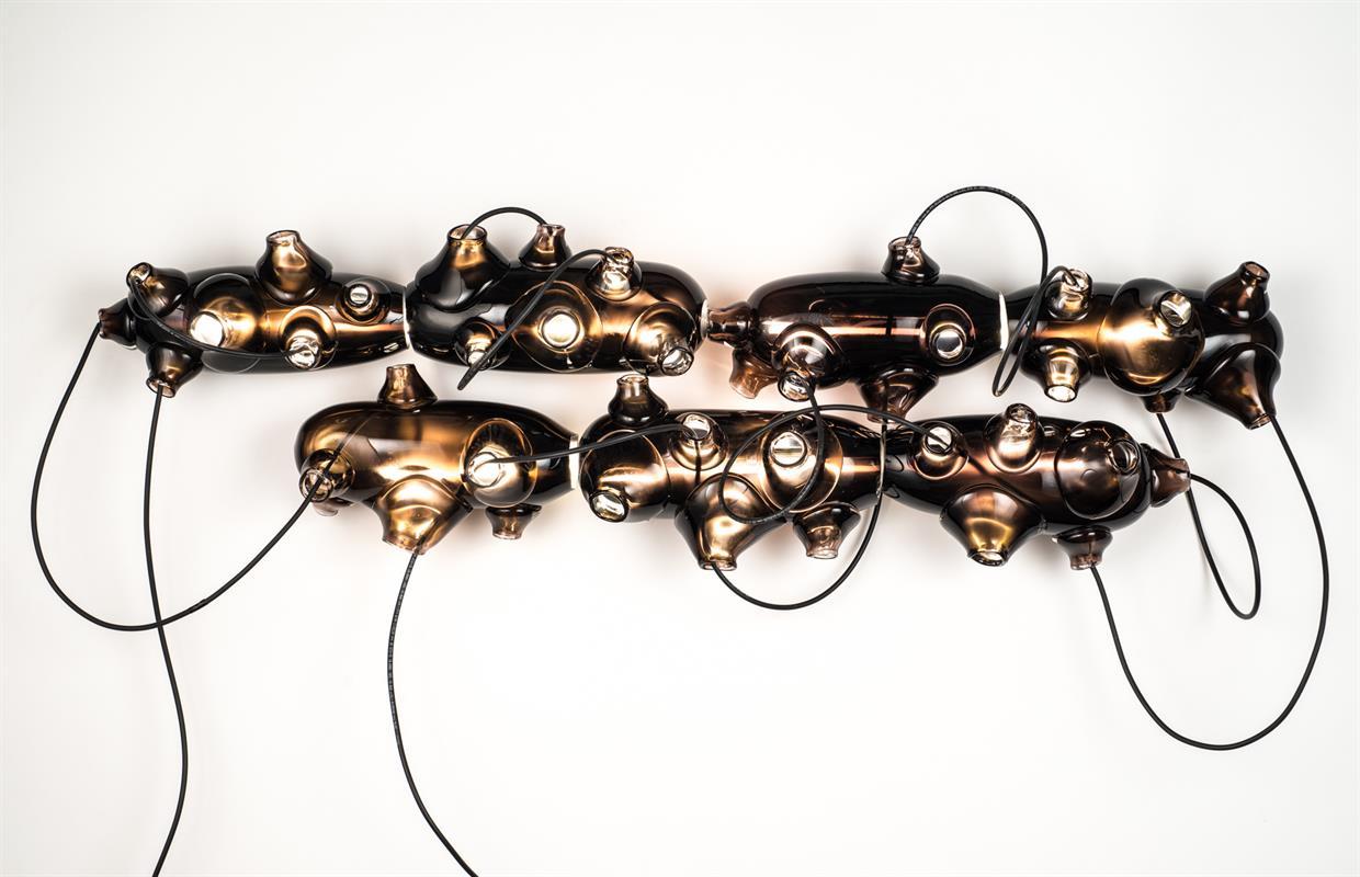 Forms were blown, cut and polished using dark purple glass. White tubes were fabricated at specific lengths and charged with argon. Argon tubes were placed inside the blown forms. Metal brackets were fabricated and wall composition was developed with cords.