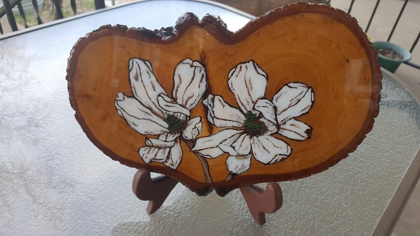 White magnolias symbolize purity and dignity they also represent the moon, any lunar goddess and for spells cast on Mondays. White magnolias are also commonly seen in bridal bouquets because the flowers are thought to reflect and emphasize the bride’s purity and nobility. A magnolia often symbolizes Yin, or the feminine side of life. French botanist, by the name of Pierre Magnol, helped scientists determine that plants came in families and not just species. Guess who magnolias are named after? That guy. Magnolias grow on trees, not vines, bushes or on stalks. These trees can live for a full century. Magnolias are thought to be one of the first flowering plants to evolve on Earth. Detailed colored woodburnig Epoxy resin finish to prevent color dulling, fading or chipping.