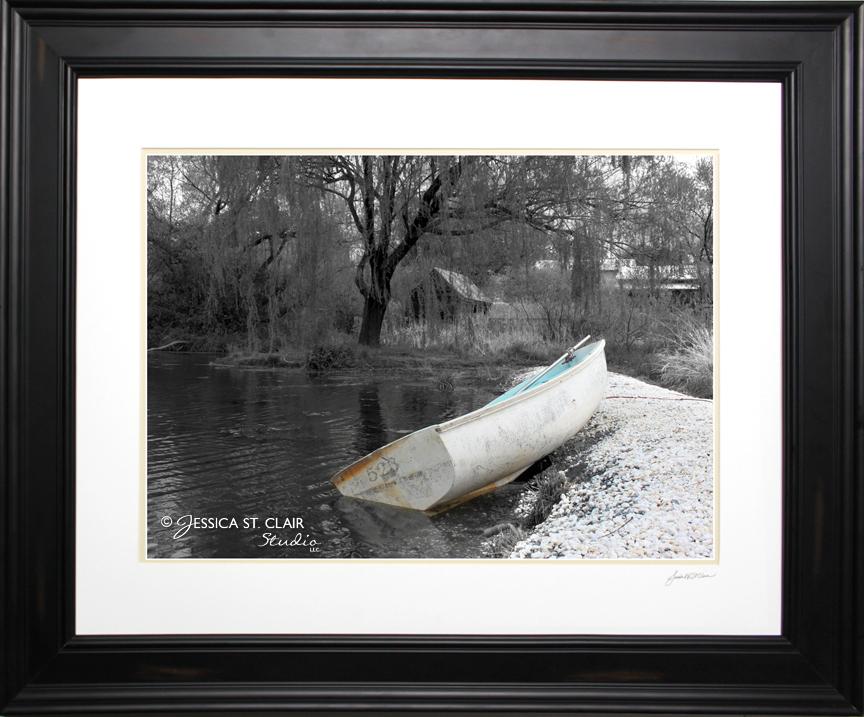An aged row boat set aground on the shoreline awaits its next passengers while a willow tree graces the water's surface in this peaceful setting. Subtle yet striking with gentle touches of blue and beige introduced against a monochrome backdrop.