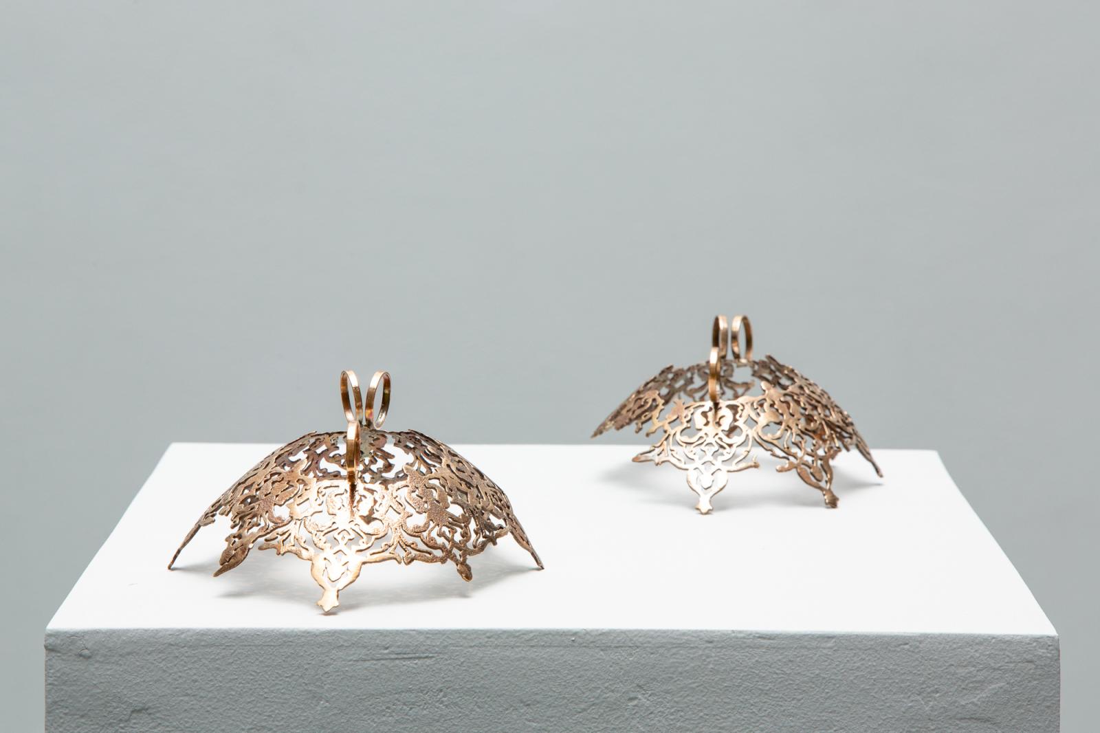 Artist Sera Boeno culminates six years of artistic exploration about gender-related power struggles in “Kelimeler Kıyafetsiz (:Words Naked/Are Not Enough)”. Using her native Turkey as inspiration, the focal point of Boeno’s exhibition is a sculptural installation adapted from the altar of Pergamon, a masterpiece of Hellenistic architecture excavated from Bergama in the Ottoman Empire (Izmir in current day Turkey) and currently held by the Pergamon Museum in Berlin, Germany. Emblazoned with quotes from Turkish media about women, Boeno’s monument serves as a stage for female performers wearing bronze ornaments of domination and torture that are embellished with delicate patterning found in Turkish illuminated manuscripts and textiles. By casting her performers as literal “pillars” of a monument dedicated to female subjugation, Boeno considers the myriad ways in which power dynamics are made manifest, whether through the essentialization of the East by the global West, or through the silencing and omission of women from representation; a story that is neither new, nor one that is exclusive to Turkey.