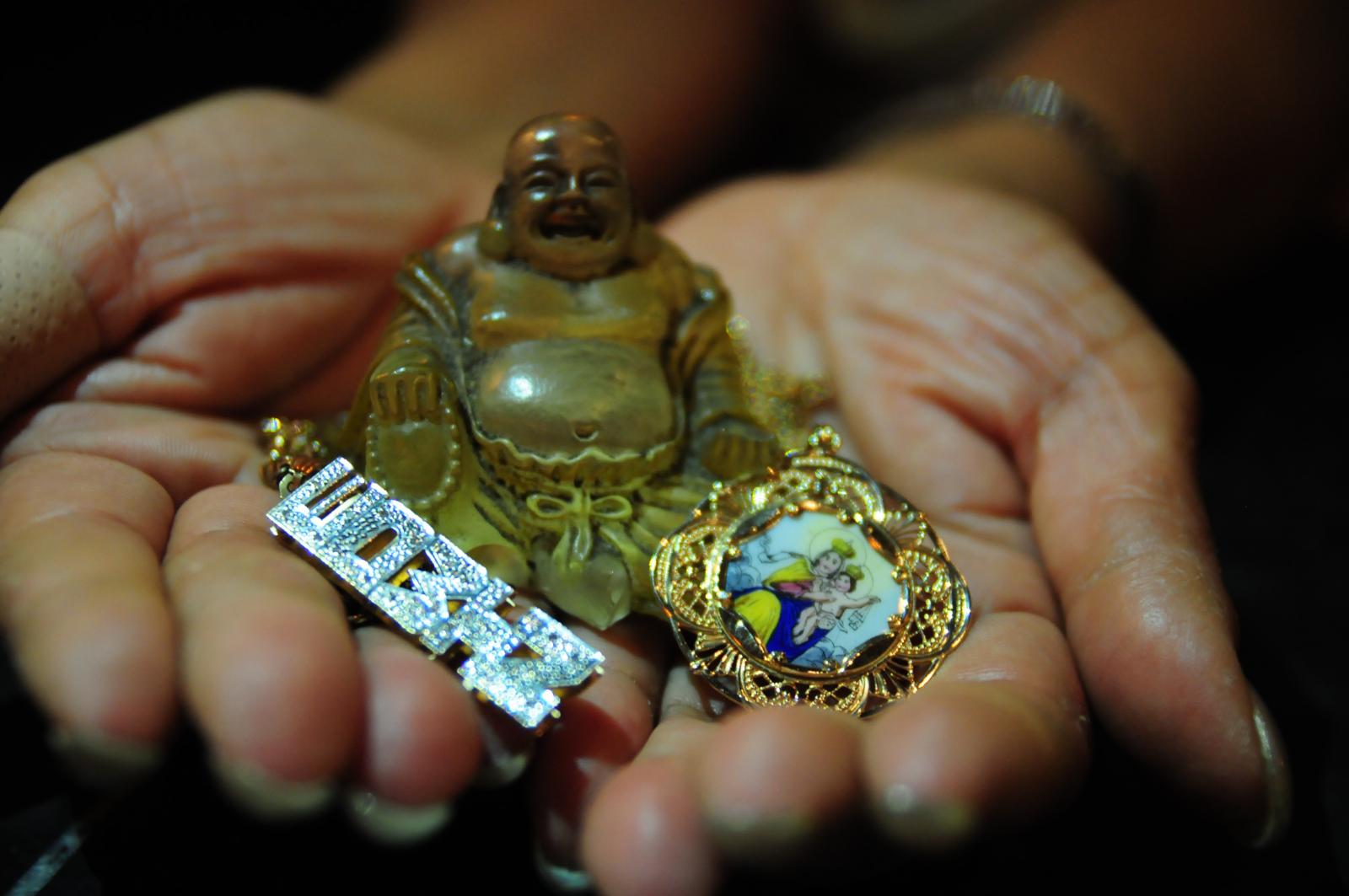"An Offering" is 1 of 15 digital images from the photo series entitled, "Relics of My Father" an evolving photography & culture project Christina Delgado uses as a form of art therapy after losing her father suddenly in 2013. The hands holding the objects belong to her Tia Evelyn who is her father's sister. The objects include her father's gold & diamond nameplate, a small Buddha statue, and a gold and enamel pendant of the Virgin Mary & Jesus which belonged to her grandmother, her father's mother.  The nameplate signifies 80's & 90's culture in NYC and offers a glimpse of Delgado's father's name. The Buddha represents wealth, peace, and a sense of humility.  The pendant is a representation of history and colonial influence on Latinx culture. 