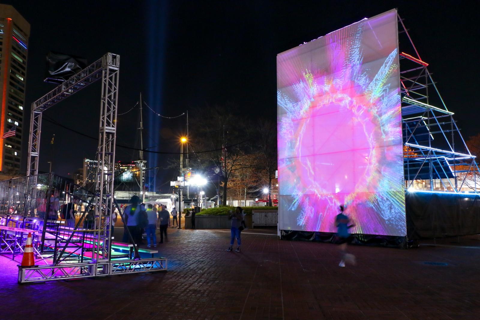 Sun Stomp
http://grahamprojects.com/projects/sunstomp 
Scaffolding, bleachers, solar panels, solar hardware, projection screen, projector, LED neon, contact microphones, video processor
34’x24’x75’
Light City Baltimore, McKeldin Square, 101 E. Pratt Street, Baltimore, MD 21230
Sun Stomp was a solar-powered light and interactive audio-visual environment that featured an interactive projection on one side and an array of sixteen 290 watt solar panels on the other. Participants were invited to stomp on the bleachers to trigger sun-inspired visuals and amplified sounds of the Sun.
April 14-21, 2018
Project partner: Baltimore Office of Promotion and the Arts