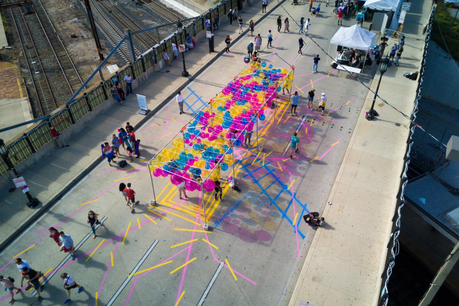 Choose Your Own Adventure
https://grahamprojects.com/projects/adventure-artscape/ 
https://vimeo.com/286601636 
Beach balls, line striping paint, tent structure, LED lights, poetry
12’x40’x100’
Charles Street Bridge at Penn Station, Artscape, Baltimore, MD 21201
Choose your own Adventure transformed Baltimore’s Charles Street Bridge into a colorful playscape of pedestrian pathways and hanging beach balls. The project was commissioned by the Baltimore Office of Promotion and the Arts for the free 2018 Artscape festival. Spray chalk lines marked a site-based map converging under a forest of beach balls hanging from an open air structure.
July 20-22, 2018
Project partner: Baltimore Office of Promotion and the Arts