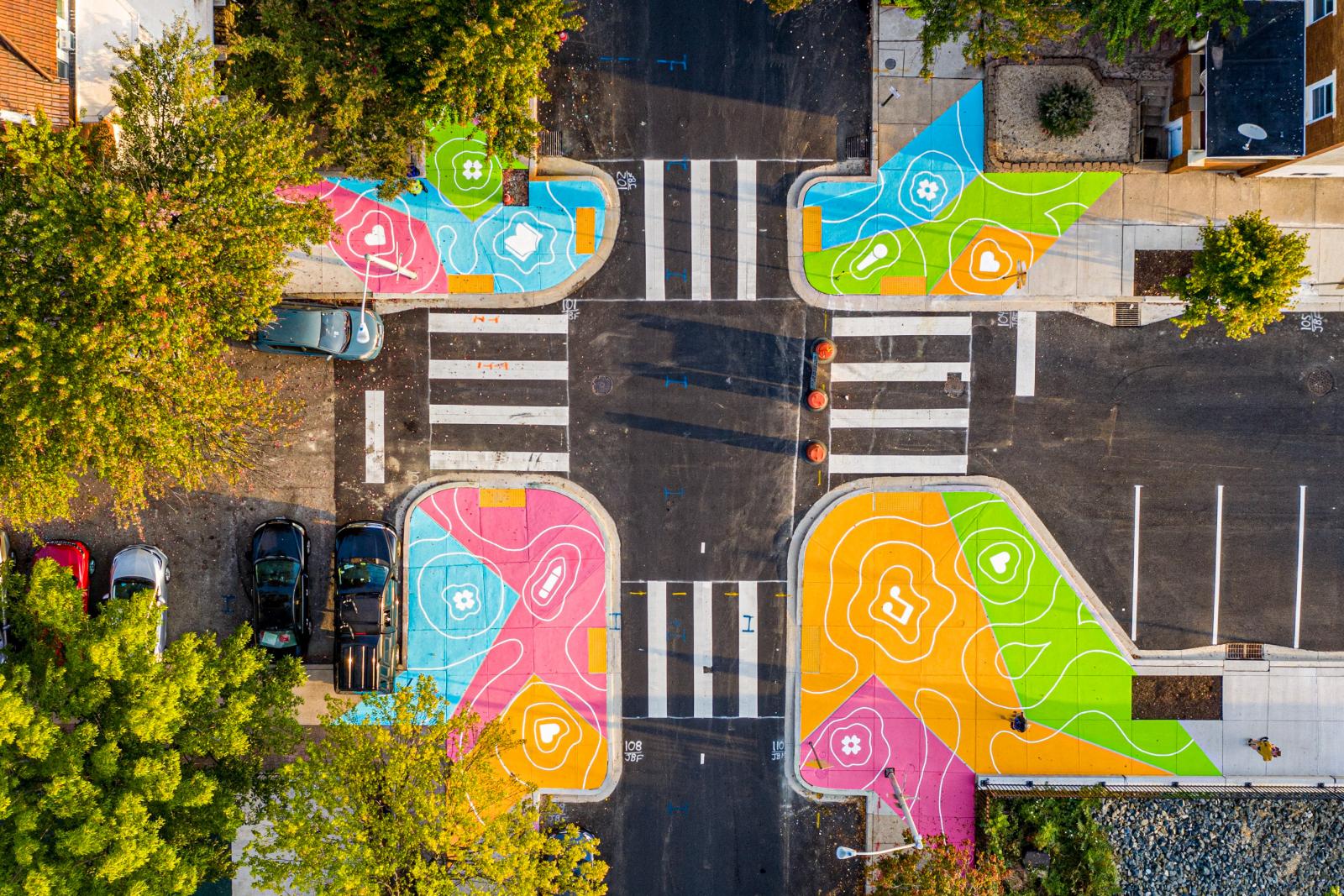 Reverberations Crosswalks #2
https://grahamprojects.com/projects/reverberations-crosswalk-calvert/ 
Federally-specified traffic paint, crosswalk, concrete bumpouts
26th St. & Calvert St., Baltimore, MD
100’ x 100’
The Reverberations Crosswalk is a pavement mural that enhances pedestrian safety for children and residents walking to Margaret Brent Elementary while celebrating the school’s art education focus. Coreil-Allen led a student drawing workshop to inspire the design and facilitated volunteer painting.
September 2019
Project partners: Friends of Margaret Brent, Live Baltimore, Margaret Brent Elementary/Middle School, the Harwood Community Association, the Charles Village Civic Association, and Baltimore City Department of Transportation
