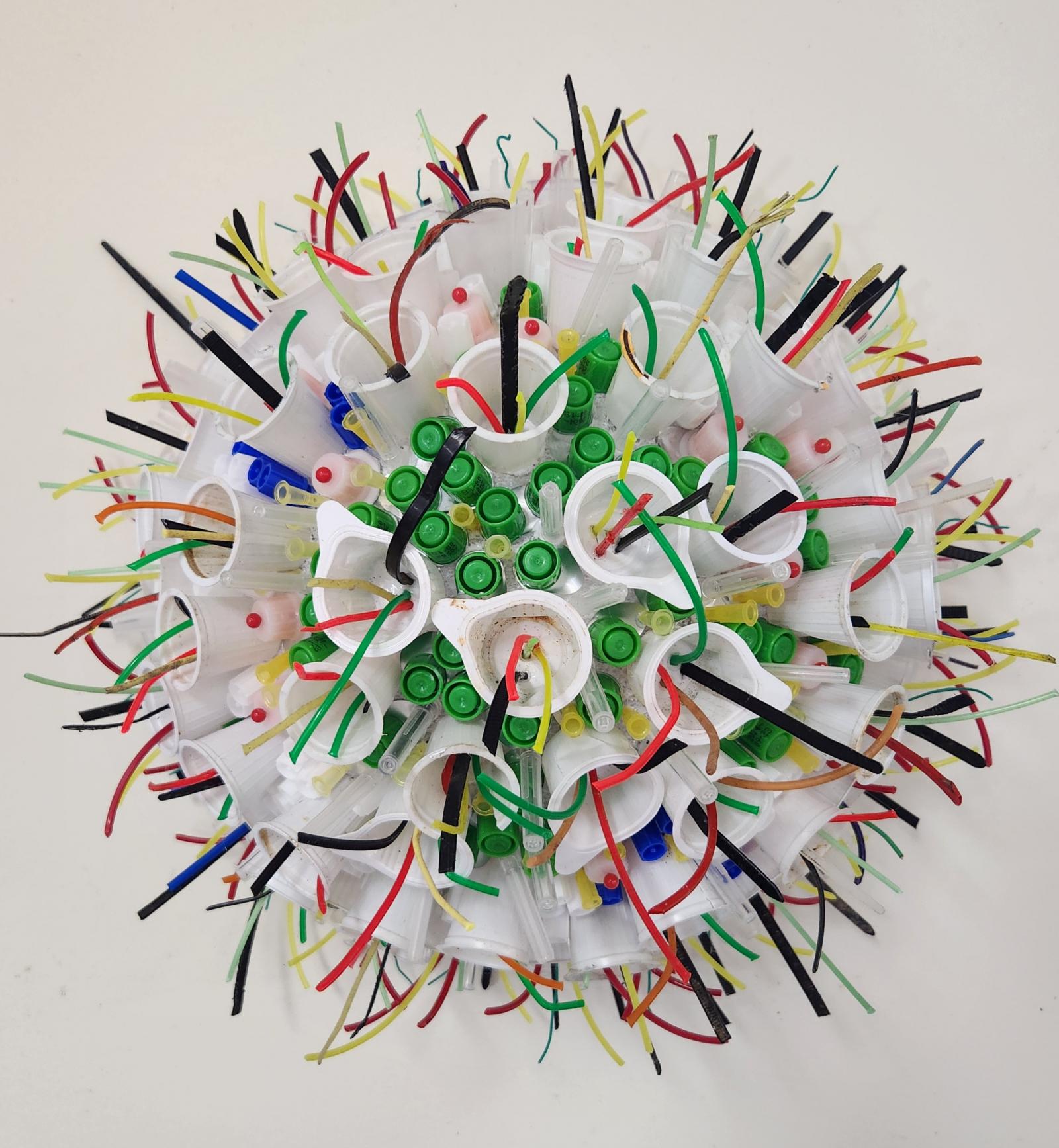 The artwork is a riff on the Covid 19 cell. A half-sphere of Styrofoam anchors a collection of found, repurposed objects: milk coffee creamers, creamer pull-tops, syringe caps, yard trimmer wires and stick pins. It measure app. 10" in diameter and is wall-hung.