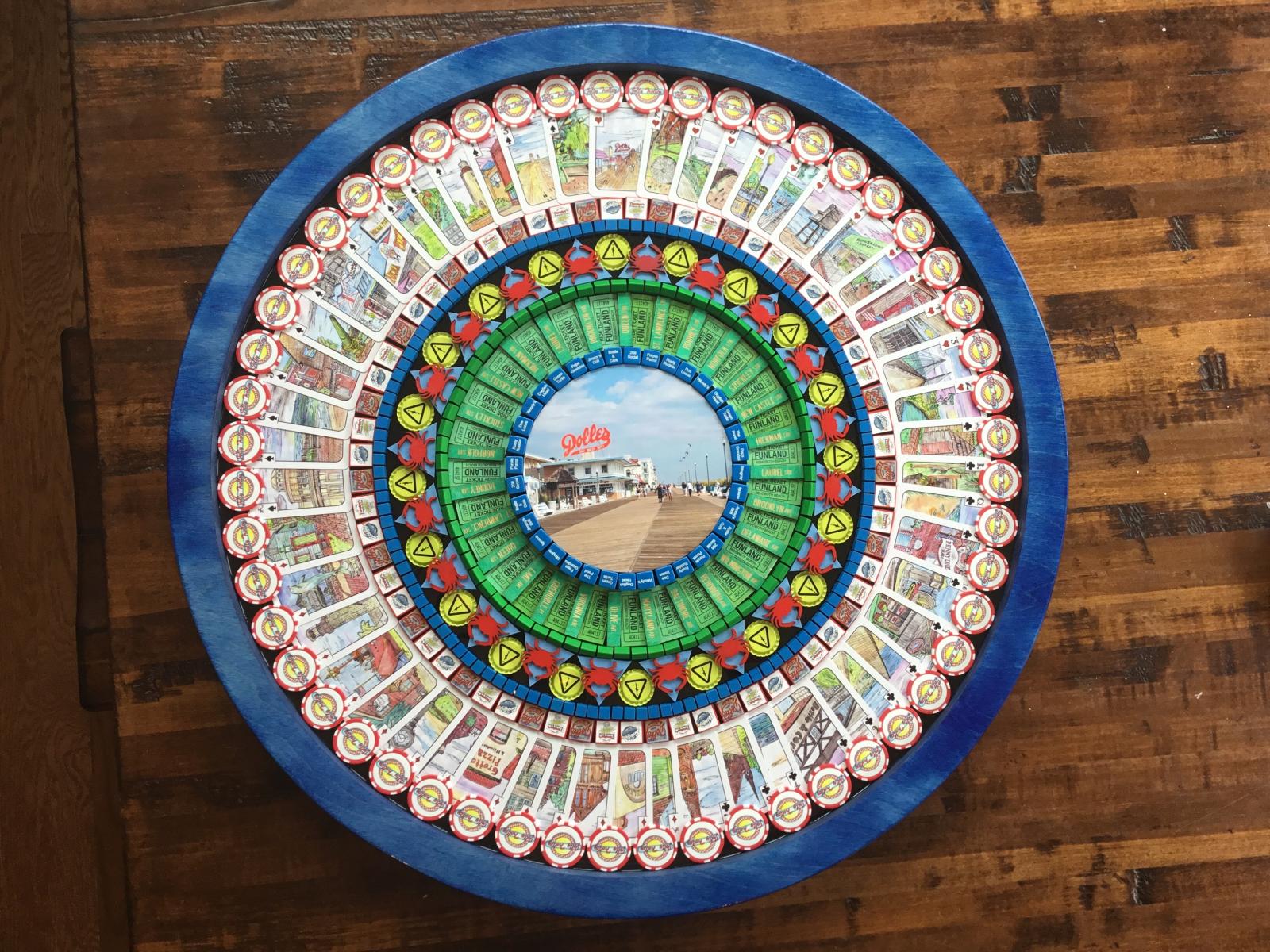 This 36 inch diameter nostalgic collage is is titled, “Rehoboth Blues”, and is composed of hundreds of items that are iconic from the Delmarva region.  The view as we walk down the Rehoboth Beach boardwalk forms the center of the work surrounded by eateries from Dewey and Rehoboth Beaches.  Pieces such as Rehoboth street signs, Funland tickets, Thrashers Fries and Jolly Trolley are meant to evoke memories of summer nights walking the boardwalk. I hunt for unique pieces from the past and assemble them into complex collages of texture and color creating  “Nostalgic Art.” Although many pieces are vintage, others I create by hand at the Baltimore Foundery. Each piece is positioned strategically to create a pattern that draws the work together. Planning takes several months for a new design. Assembly begins in the center and I work outward with construction taking place over several weeks. The completed pattern is then sealed using multi-layer epoxy resin, which creates shimmer and protects the work.  The resin also allows you to trace your fingers over the different textures, for both a visual and tactile experience.