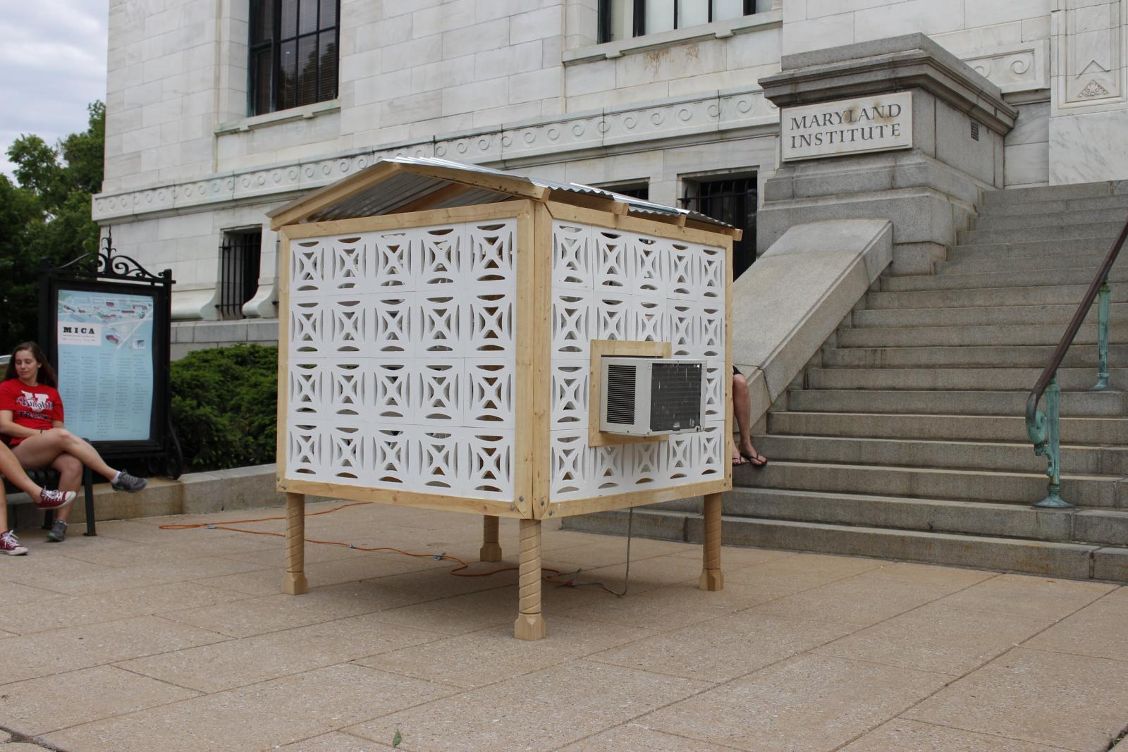 Gracias, a site-specific structure that resembles a small shed, makes use of standard tropical architectural imagery and an attached air conditioning unit to portray ineffective design. Its walls, made to mimic concrete ornamental blocks commonly found in the Caribbean fail to contain the cooled air that the unit provides. The air conditioning unit, in turn, derives its power from a larger structure that dwarfs Gracias, and reiterates the prevalent relationship between Puerto Rico and the United States.