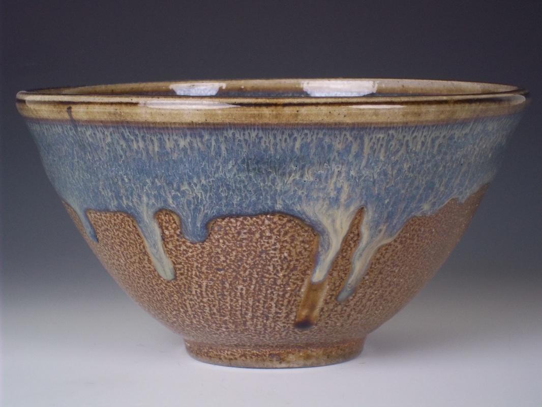 A functional stoneware bowl fired in a wood-fired kiln with wood ash deposits which was then refired in a soda kiln for a glossy, metallic finish.