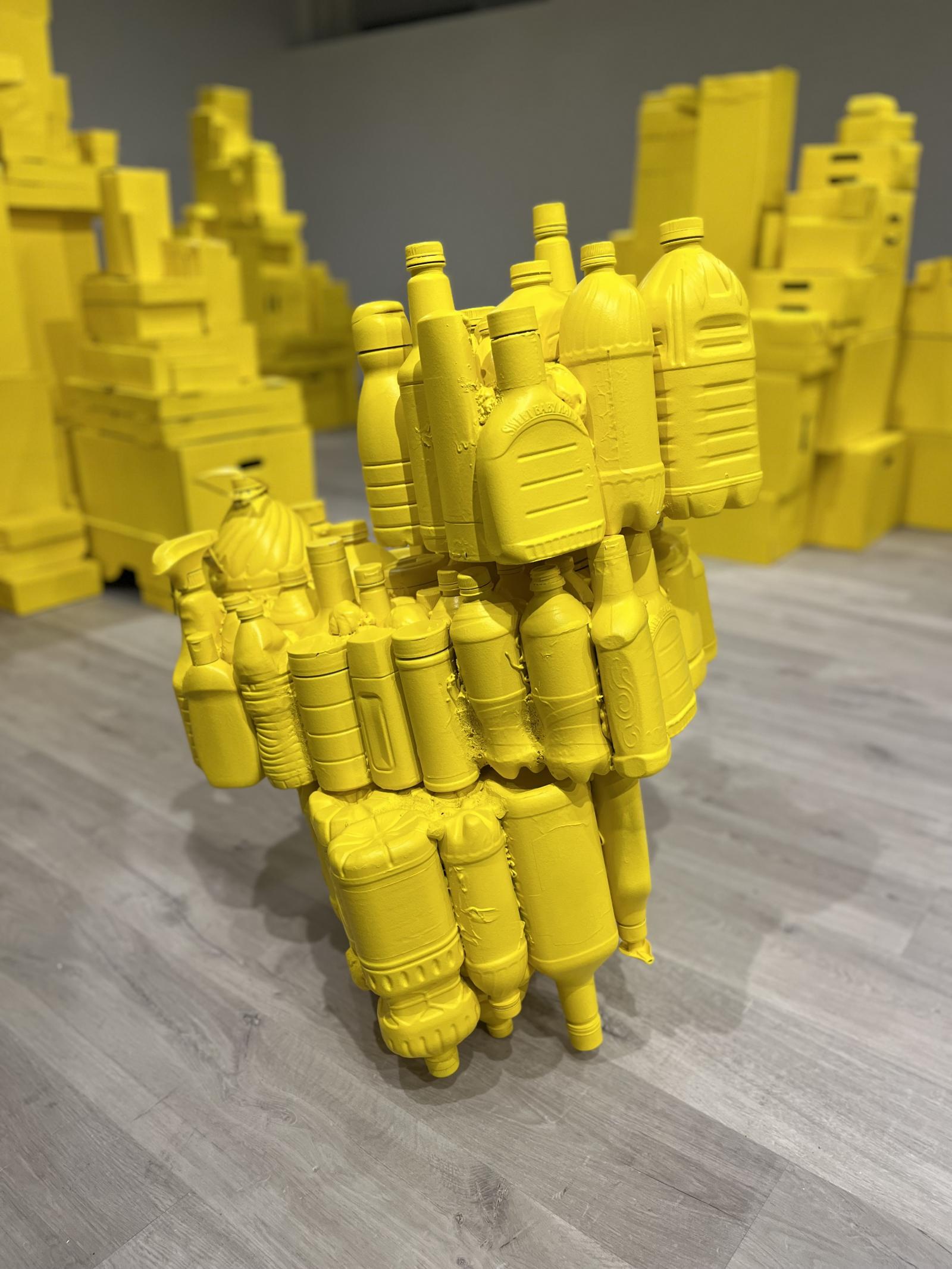 "Plastic" is part of a solo show in Gallery 194 at the Chesapeake Arts Center. The piece is made of recycled plastic collected from January 2022 to January 2023. The plastic items are fused together and painted a solid yellow color. "Plastic" is one of two pieces installed in the show "The Essentials" which is on display from Jan 12- Feb 13, 2023. This image is a detail shot of the piece "Plastic". Each section of the work is for sale for $300 a piece and $1500 for the entire collection.