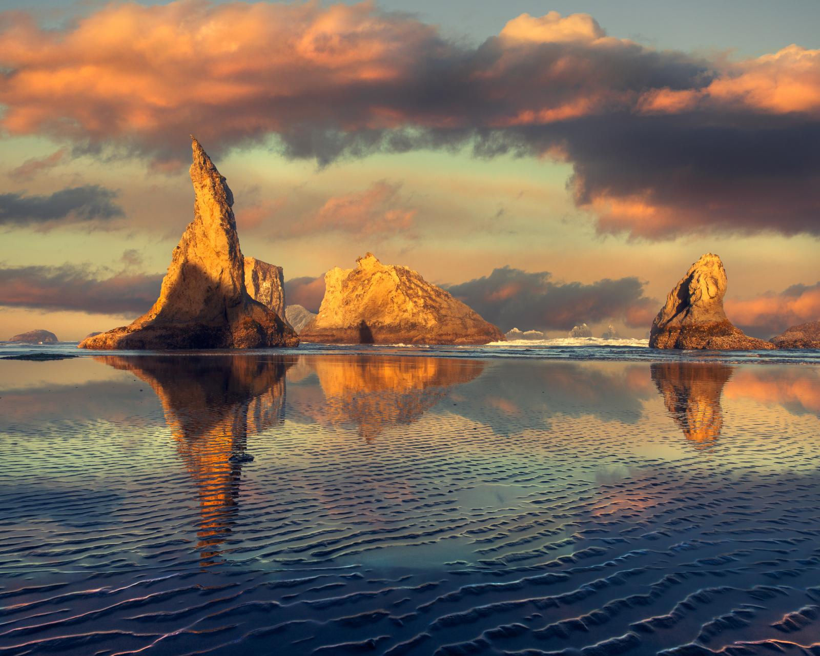 Waking before dawn along the Oregon Coast for sunrise is always special. The sand under your feet is fresh, as the tide has washed away all the footprints from the previous day under the cover of night. And it's always a great morning when your eyes and mind get the opportunity to stare into the mesmerizing sights and sounds of the Pacific Ocean's waves crashing upon the rugged shoreline, while your body soaks up the wet, sea-salt air as it breezes through you and delicately leaves its salt residue upon your soul.
Many of you know (either as Oregonian's or people who have visited), scene’s like this one, on any morning, might mean the absent of the sun and its light; as the lush, green state of Oregon and its coastline has many overcast mornings. So, when you wake and find that the clouds are parting and the brightness of the sun’s rays will be beaming its gorgeous tones upon the rock croppings of Bandon’s pristine beach line, you're giddy like a child. You smile at the rocks. You skip in the sand. You talk to the waves. And hope that something, anything can hear and share this beautiful moment in time with you. And although there wasn’t a physical person along the shore on this morning, I felt like the souls who have gone before me where near as I was squatting within in the wetness of the beautiful textures of the sand ripples left behind by that overnight tide.