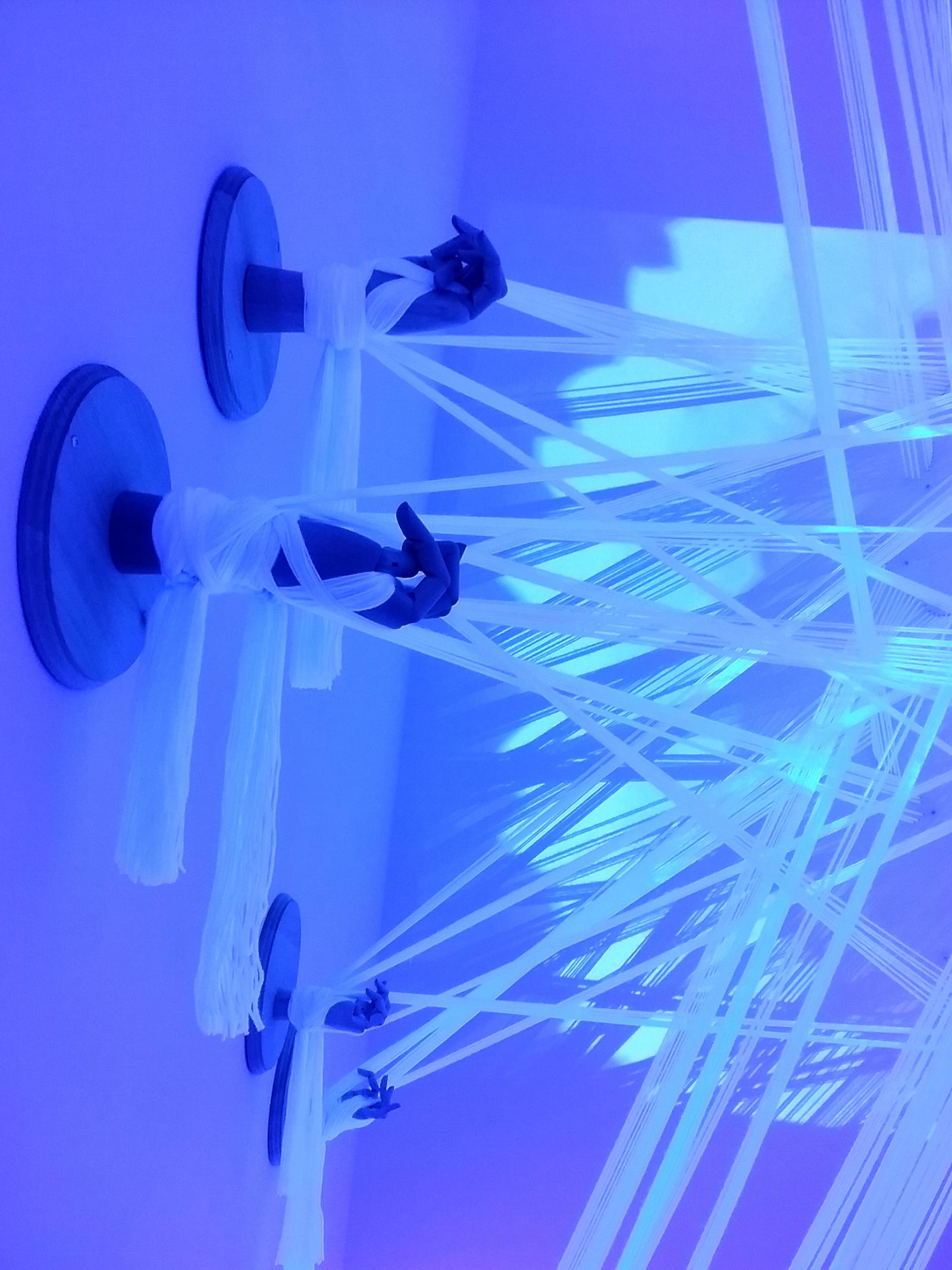 Revealuxion, a multi-media installation by Kieun Kim, utilizes mechanisms and forms inspired by butterfly chrysalides and stringed marionette hands. With this work, Kim envisions herself through the reflection of a chrysalis — a metaphor which embodies the suffering and vulnerability, as well as the patience and self-determination required for periods of intense personal growth. For the artist, the process of making and presenting Revealuxion to viewers is an exercise in unapologetically embracing and revealing the genuine self, forgoing the propensity to put forth inauthentic versions of ourselves to the people we encounter. The patience inherent with this work is reflected in the details — which feature kaleidoscopic projections, laser cut acrylic, articulated wooden hands, and hundreds of yards of carefully stretched, illuminated cotton string.