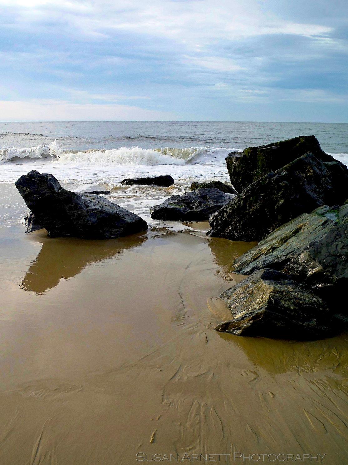 The early morning tide rushes back out to sea among the rocks, storm clouds gathering behind it, in Cape May, New Jersey.