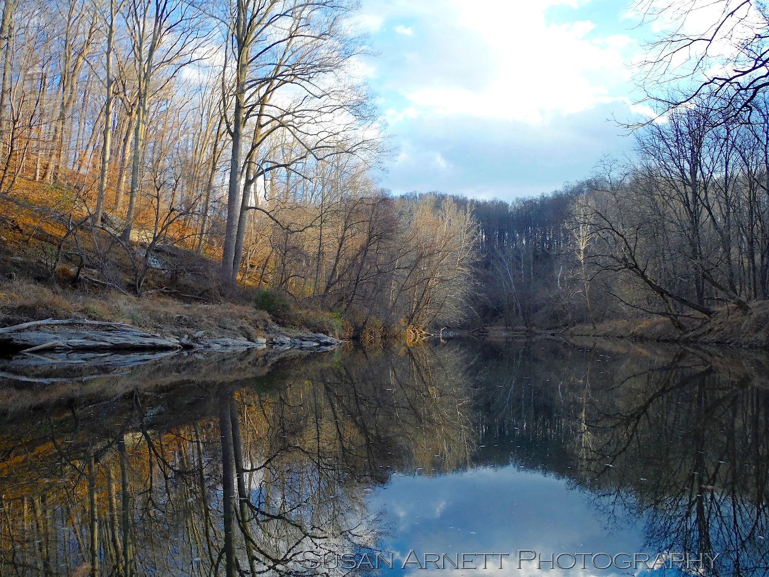 The sun sets across the Patapsco River Valley in Maryland among the bare trees of late fall.
