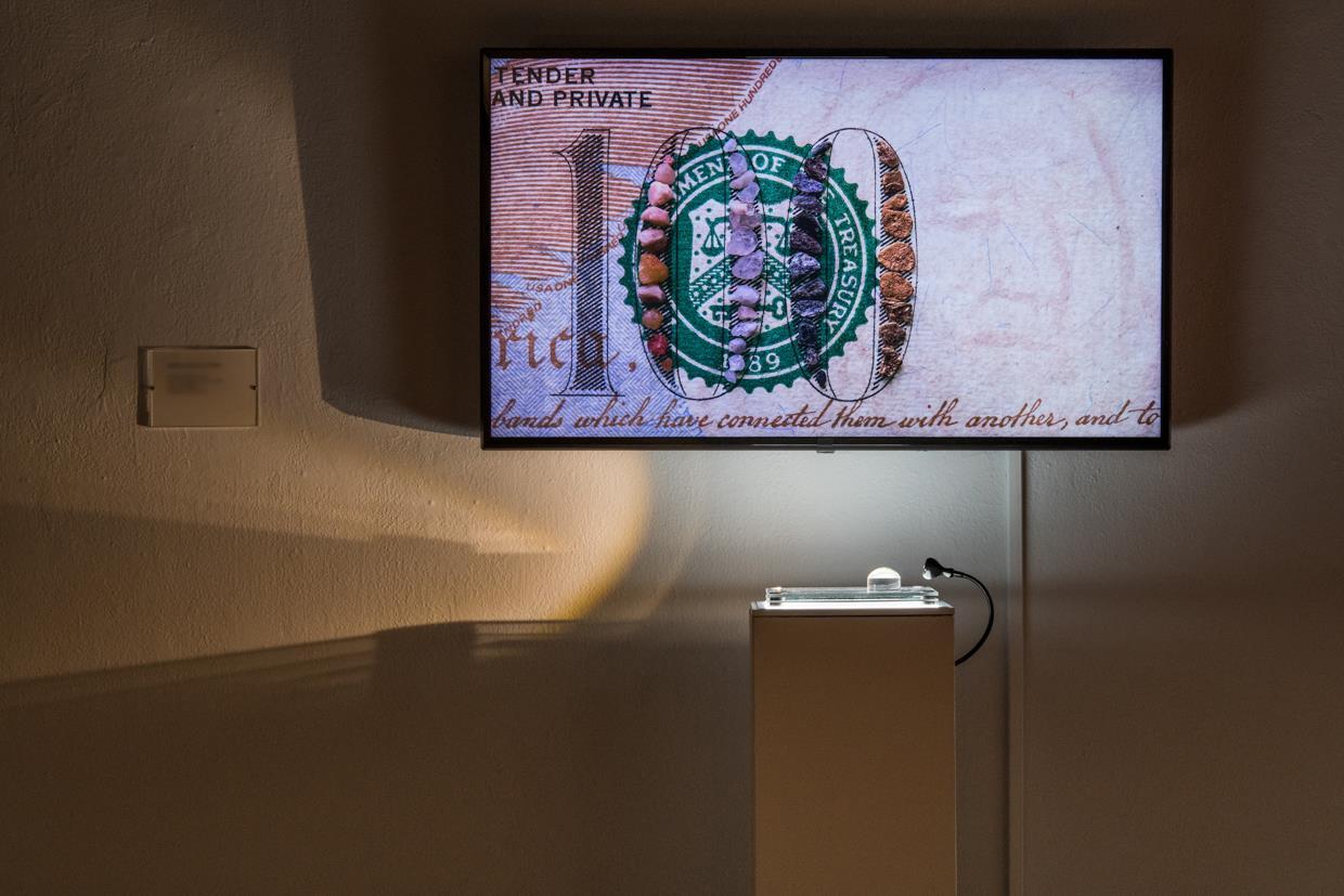 Shot at micro level on a $100 bill, grains of sand group, dissolve, and regroup in an endless cycle. The 10 second video plays on a 4K monitor above a sculpture of the work on a light pedestal with a magnifying globe, inviting the viewer to look closely at the details of individual grains of sand.