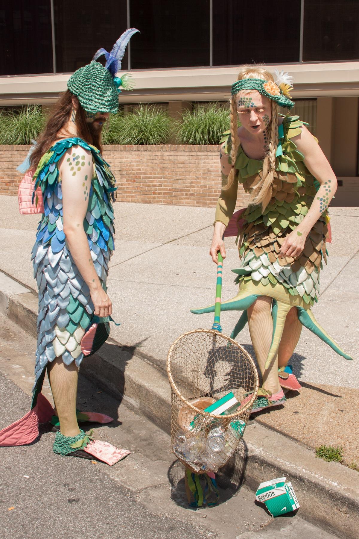 A walkabout performance featuring two centuries-long residents of the Chesapeake Bay who have left their native waters in order to understand the source of its destruction. In search of answers and possible solutions, they wander the streets of Baltimore, interviewing its residents, intercepting debris before it enters the waterways and crafting merfolk charms from plastic bottles. These sea-life charms serve as a kind of exchange for donations of plastic bottles from humans and their promises to help restore the Chesapeake.
PHOTO credit: Anastasia Tantaros and www.annekaphotography.com/