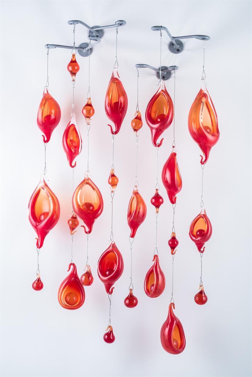 Individual forms were blown and polished. Solid glass balls were made to fit into the pieces and solid hook pieces were also created. All the pieces were connected to wire to provide space to breath. Metal Brackets were fabricated to hold the wall composition.