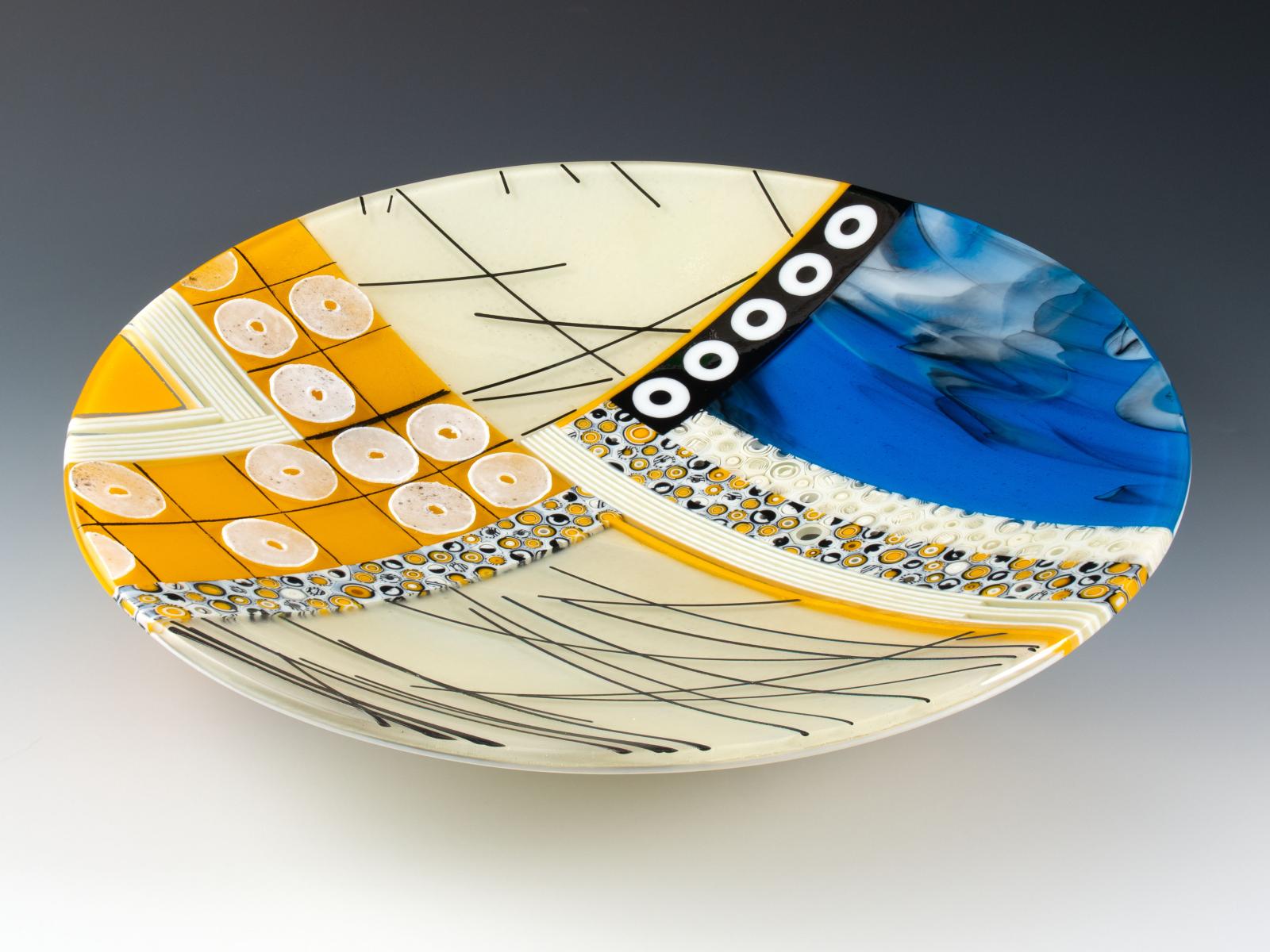 Rich blue, electric marigold, sparkling iridescence, complex patterned murrine, floating threads of glass, and raised rings of glass powder. You'll want to run your fingers over them every time you walk by.

The glass cylinders in this bowl are sections individually cut from hand-pulled glass cane which I create by heating glass to 1500 degrees and pulling it into rods while molten in a modern-day adaptation of the 16th century techniques of the Murano glassmakers.

Fused, coldworked and slumped.