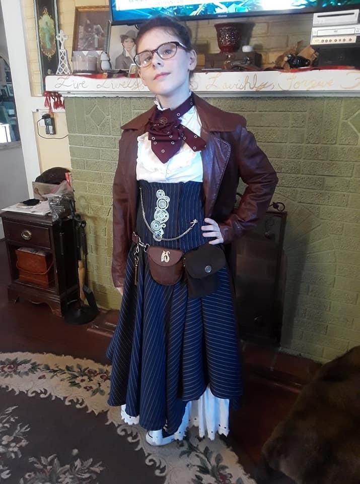 Another cosplay/costume piece made for my teenage daughter. Gender bending the BBC's famous "Doctor Who" #11. The 11th Doctor always wore a pinstriped suit, tie, glasses, converse "Chuck Taylors" and a trench coat.
We played with this idea and not only did a gender twist on it, but a "Steampunk" twist as well, with a slight nod to the Victorian. I made a waist-cincher in navy pinstripe material with machine-embroidered "Gallifreyan" language on the front and a matching full skirt. A cravat-type neckpiece was made from men's silk tie and a tie pin made from a gear to hold it in place. A thrift store leather trench coat and knee-high Converse All-Stars top off the look.