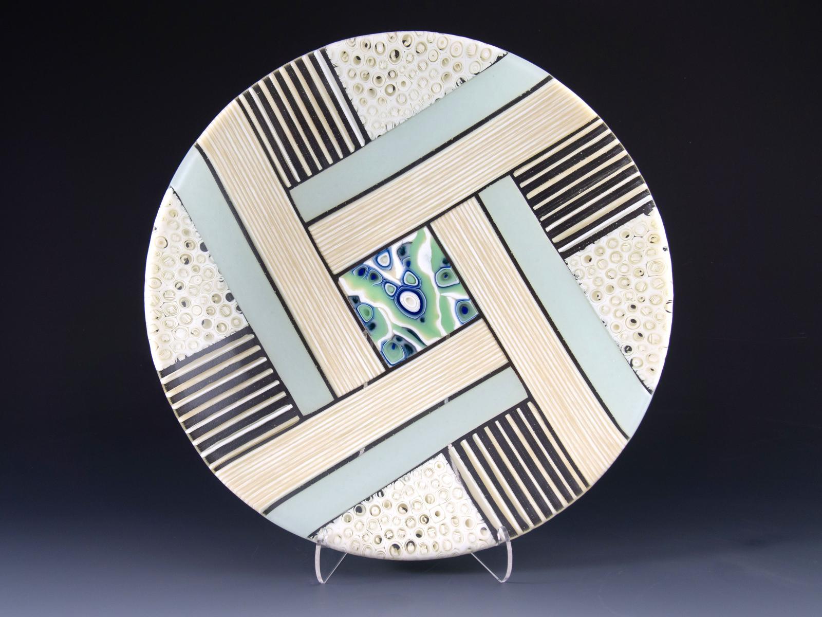 Stripes of creamy vanilla and swaths of delicate mint radiate from the scrumptious center of this shallow kiln-formed glass bowl. Patterned murrine nestle beside strips of vanilla floating in a field of clear glass that lets light shine through the vessel.

Murrine are glass cylinders, which are sections individually cut from hand-pulled glass cane, which the artist creates by heating glass to 1500 degrees and pulling it into rods while molten in a modern-day adaptation of the 16th-century techniques of the Murano glassmakers.

Fused, cold worked and slumped.